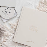 Baby milestone book with '12 weeks' milestone card on a soft textured surface.