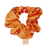 An orange scrunchie with Emma Memma character patterns and a label attached.
