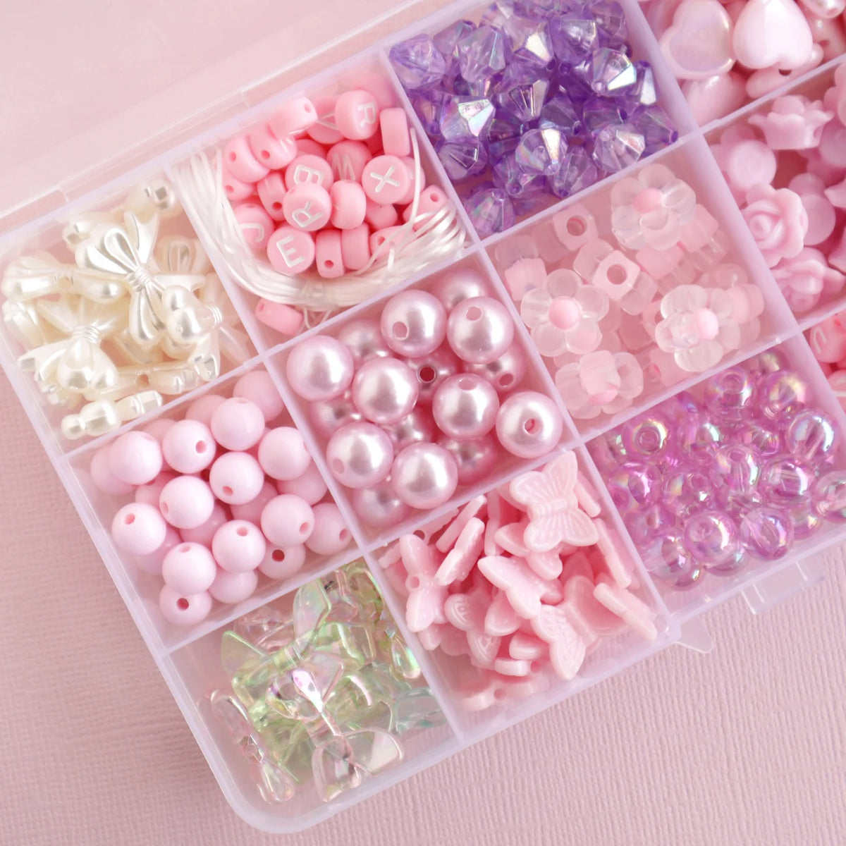 Assorted pink and purple beads in a clear plastic organizer on a pink background