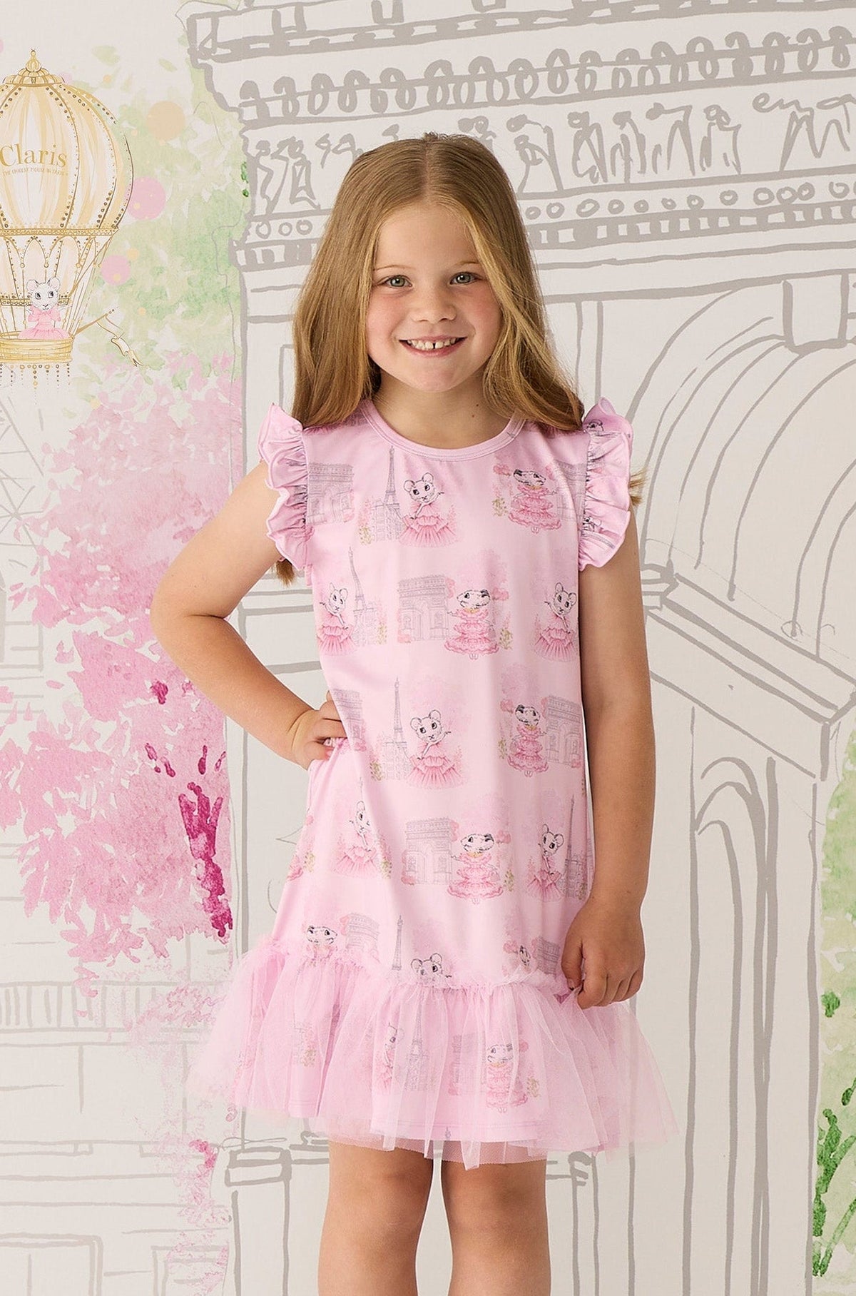 Young girl wearing a pink Claris dress with Claris the mouse pattern against a decorative wall.