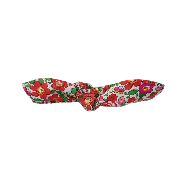 A fabric hair tie with a red and green floral pattern on a white background, tied in a bow shape, shown on a plain light gray background.