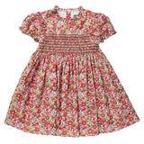 A toddler girl's short-sleeve dress with a vibrant red, pink, and green floral print, featuring a smocked bodice and puffed sleeves, laid flat on a light gray background.
