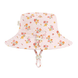 A light pink bucket hat with a colorful floral print, featuring a chin strap and a small bow on the front, set against a plain light gray background.