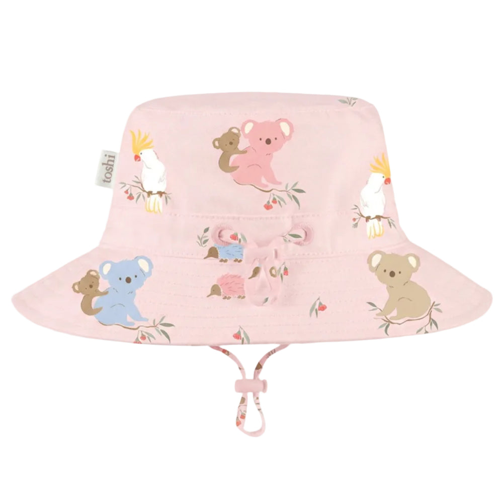 A light pink bucket hat for children, featuring a playful cartoon animal print of koalas, a pink kangaroo, a blue koala, a pink kangaroo, and white cockatoos. The hat has a chin strap with a pink and white patterned loop, shown against a solid light gray background.