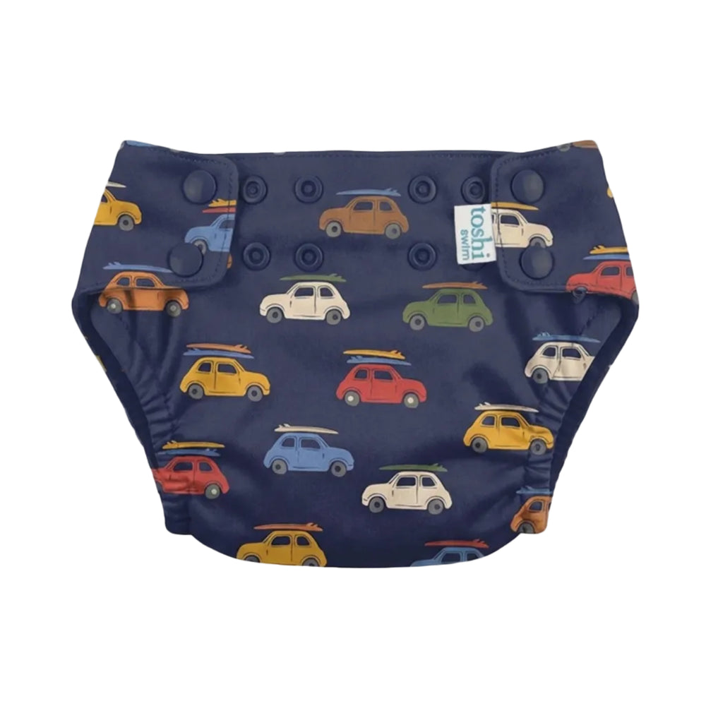 A navy blue reusable cloth swim nappy with a colorful pattern of retro cars and surfboards, featuring snap closures and a small white brand tag.