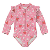 A pink long-sleeve baby swimsuit with a front zipper, ruffled shoulder details, and an all-over strawberry and white flower print, shown against a solid light gray background.