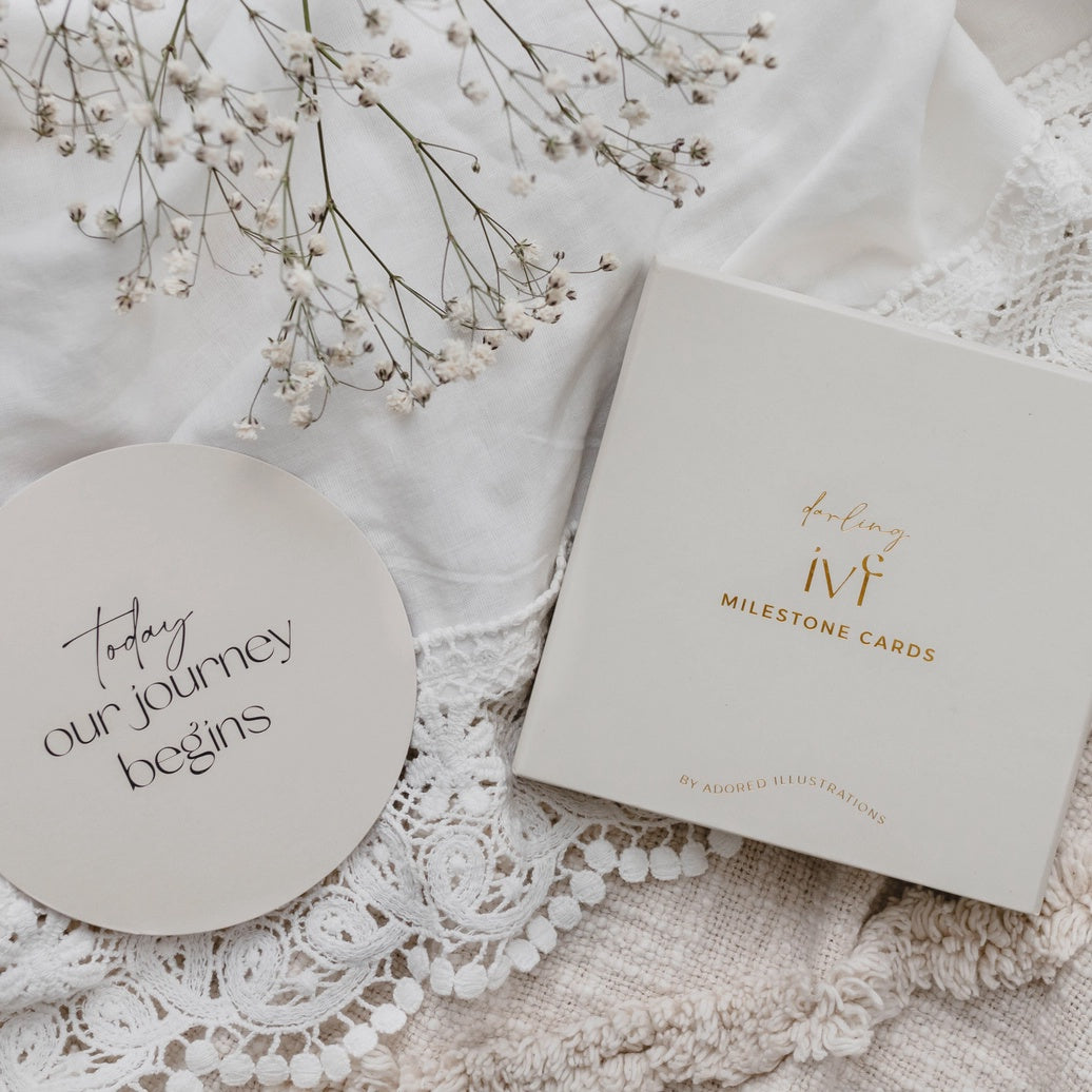 Circle milestone card with 'Today our journey begins' and a box of milestone cards on lace fabric with baby's breath.