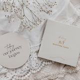 Circle milestone card with 'Today our journey begins' and a box of milestone cards on lace fabric with baby's breath.