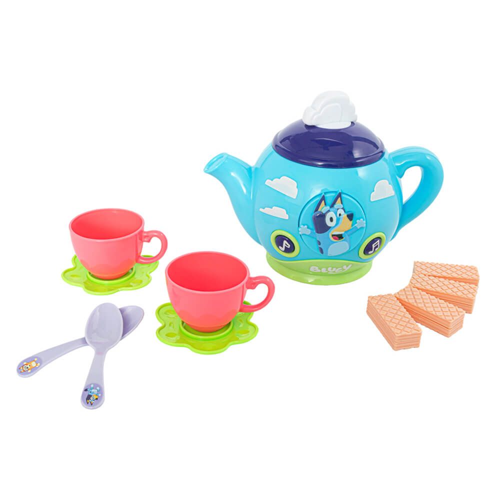 A children's toy tea-time set on a white background, featuring a light blue teapot with a dark blue lid, two pink cups on green saucers, two purple spoons, and four peach-colored waffle pieces. The teapot has cartoon character graphics and the brand name 'GABBY' visible on the front.