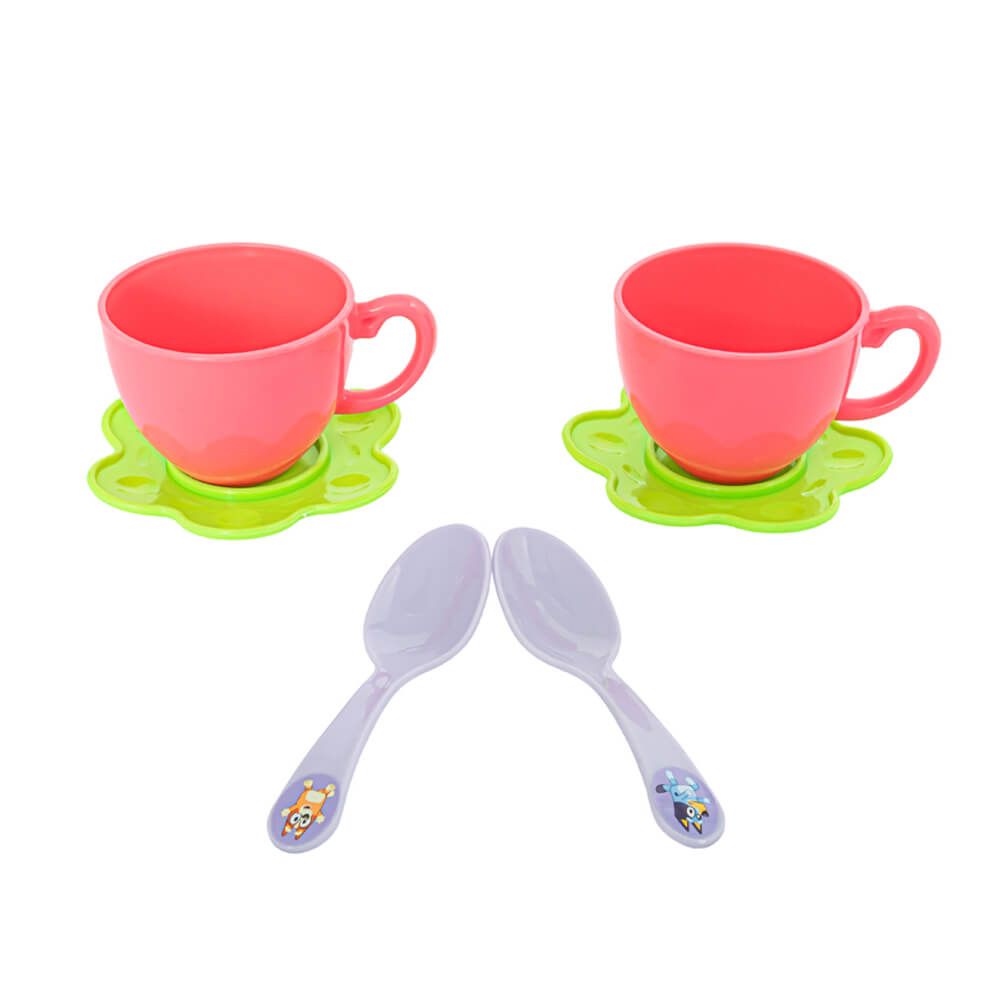 Two pink children's teacups with green flower-shaped saucers and two light purple plastic spoons with cartoon animal handles, displayed on a solid white background.