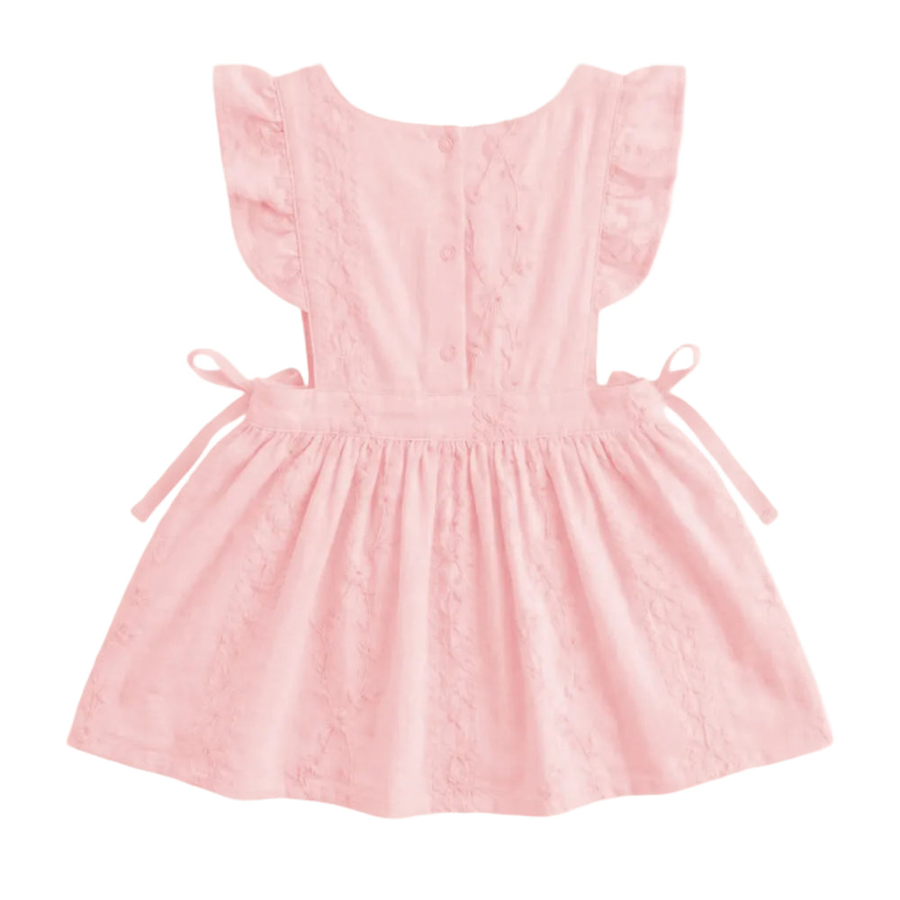 A light pink baby dress with ruffled cap sleeves, a buttoned back, and side ties, shown against a plain light gray background.