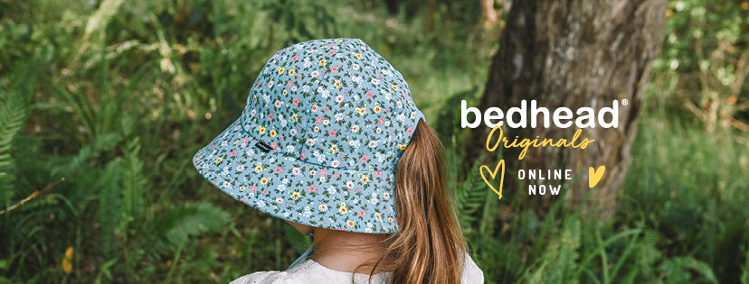 A child wearing a light blue bucket hat with a small multicolor floral pattern, photographed outdoors in a wooded setting. The brand text 'bedhead Originals ONLINE NOW' appears on the right side of the image.