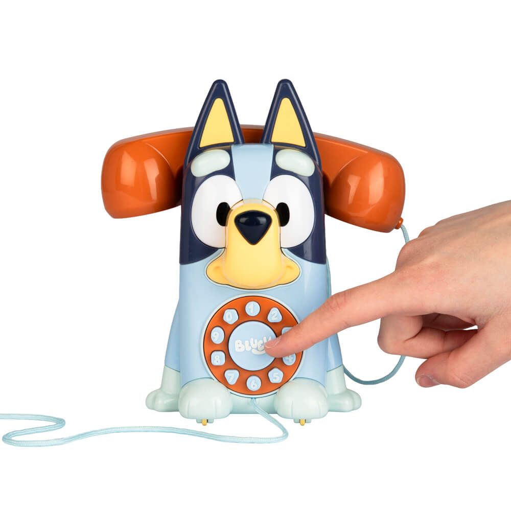 Bluey dog toy telephone with a human hand pressing the orange button, on a white background.