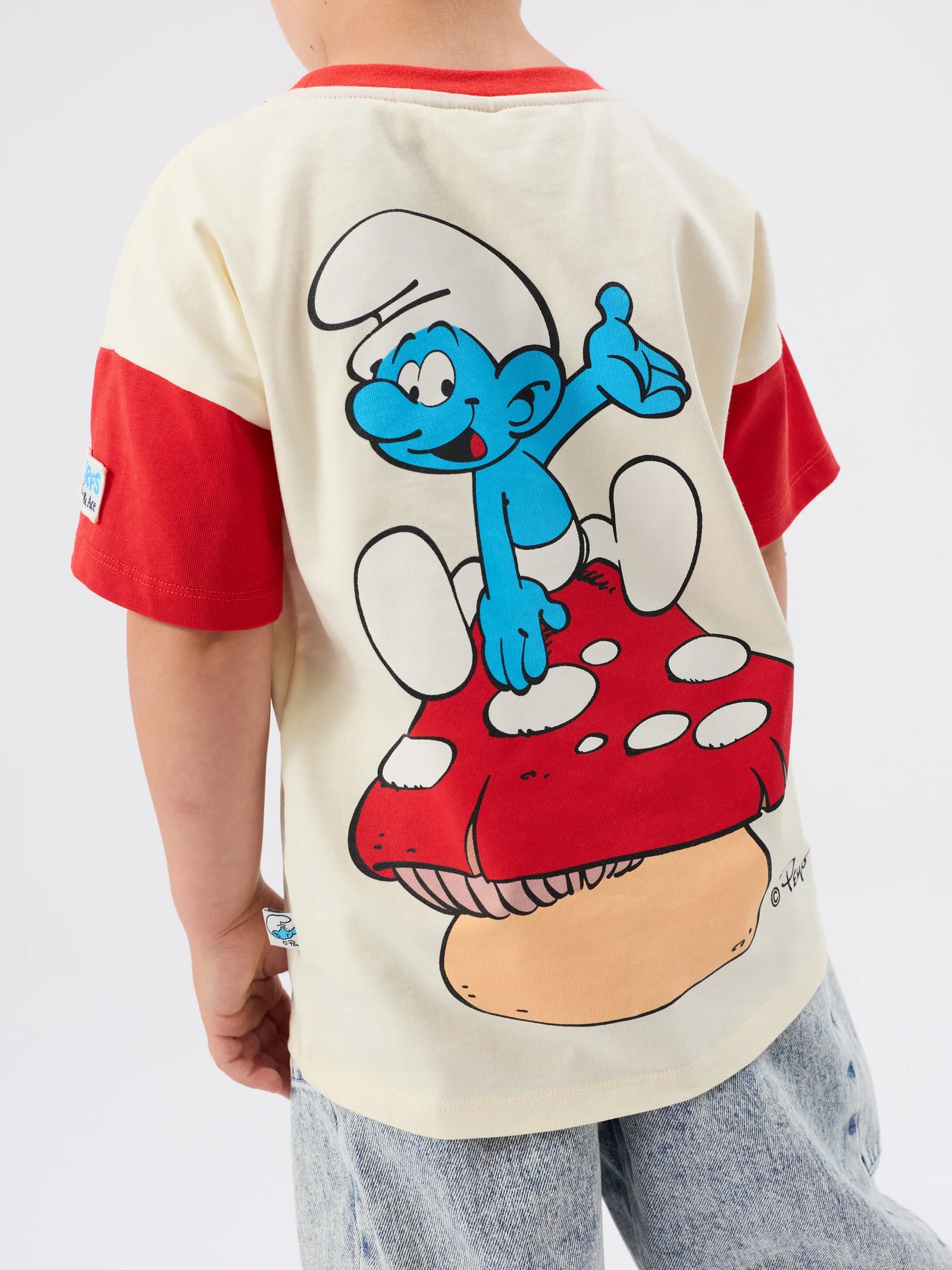 Beige t-shirt with red sleeves and a smurfs mushroom logo on a white background