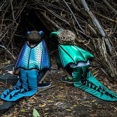 Two children in dragon costumes standing in front of the base of a tree.