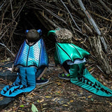 Two children in dragon costumes standing in front of the base of a tree.