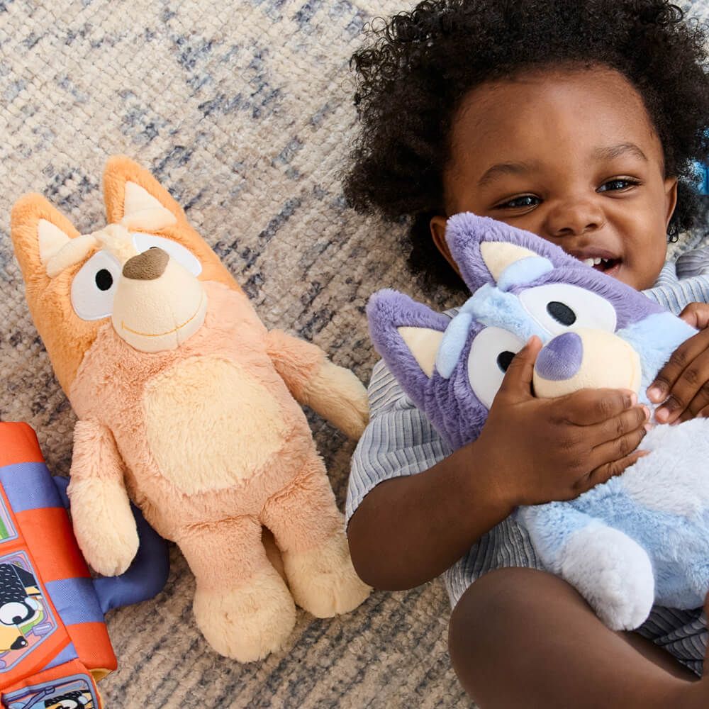 Child holding two plush toys on a carpeted floor