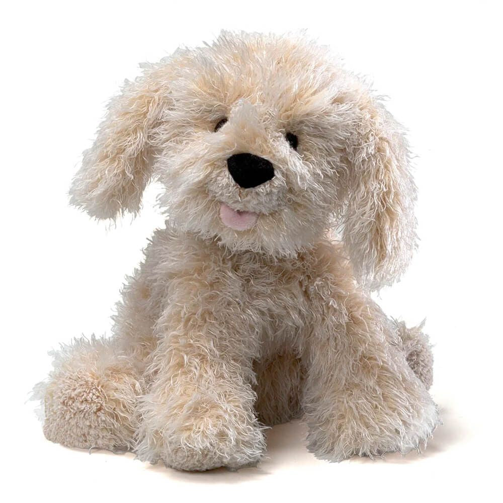 A fluffy beige stuffed  labradoodle dog toy with long curly fur, floppy ears, black eyes, a black nose, and a small pink tongue, posed against a plain white background.
