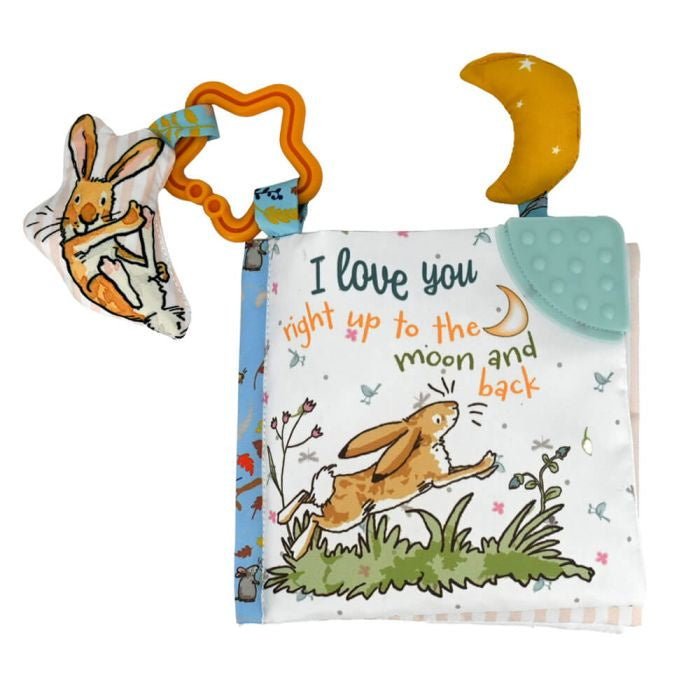A soft book with a 'Guess How Much I Love You' theme, featuring illustrations of a rabbit and a moon, along with text. The book has a star-shaped clip and a fabric attachment shaped like a moon.