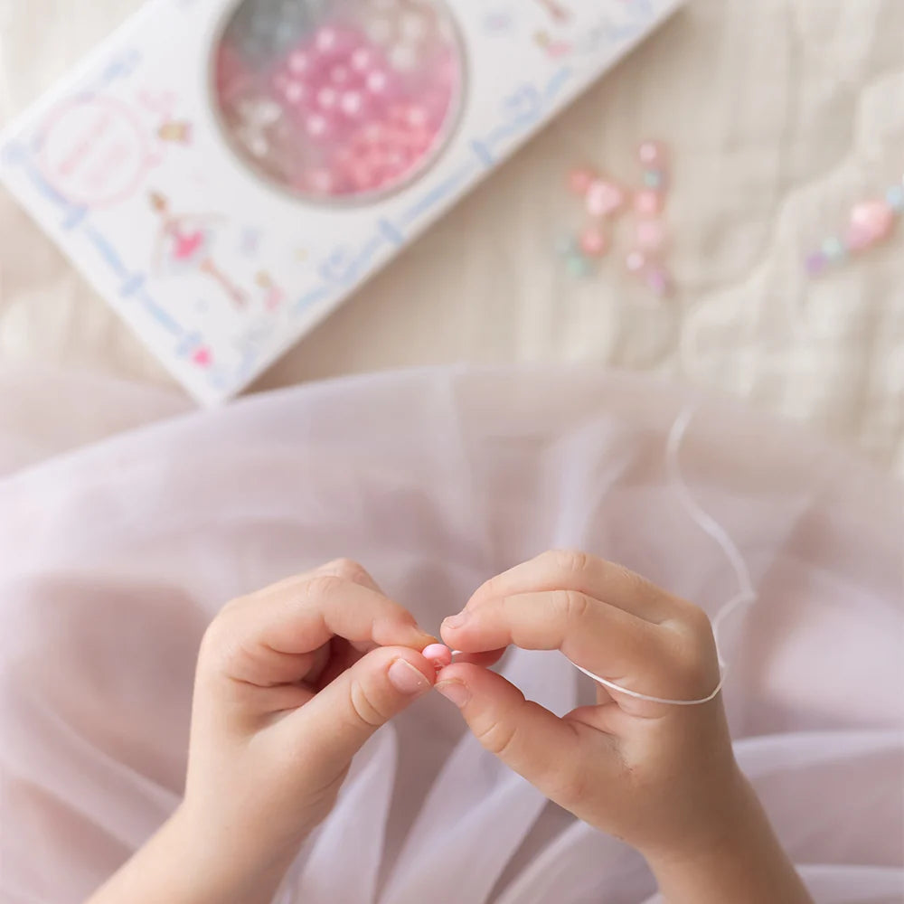 Person stringing beads on a thread with a pink bead and a tray of beads in the background.