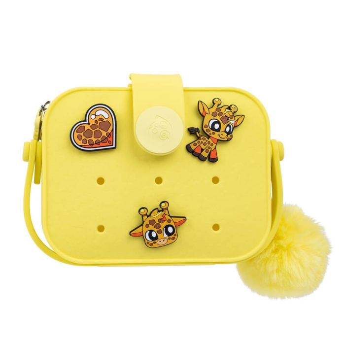A yellow handbag with a giraffe design, featuring an integrated handle, a fabric strap, and a fluffy pompom accessory, with decorative pins attached to it.