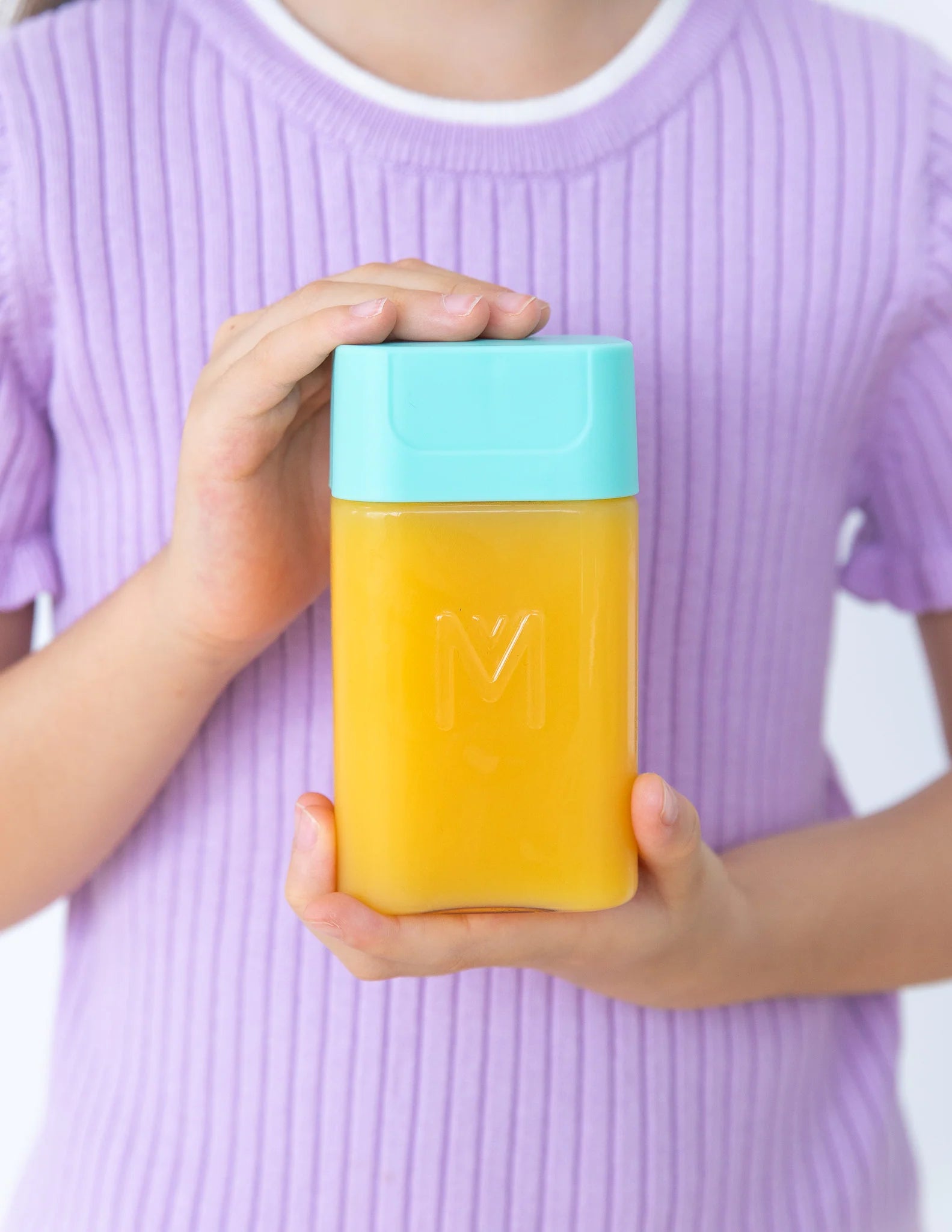 A hand holding a translucent yellow rectangular container with a light blue cap against a plain white background.