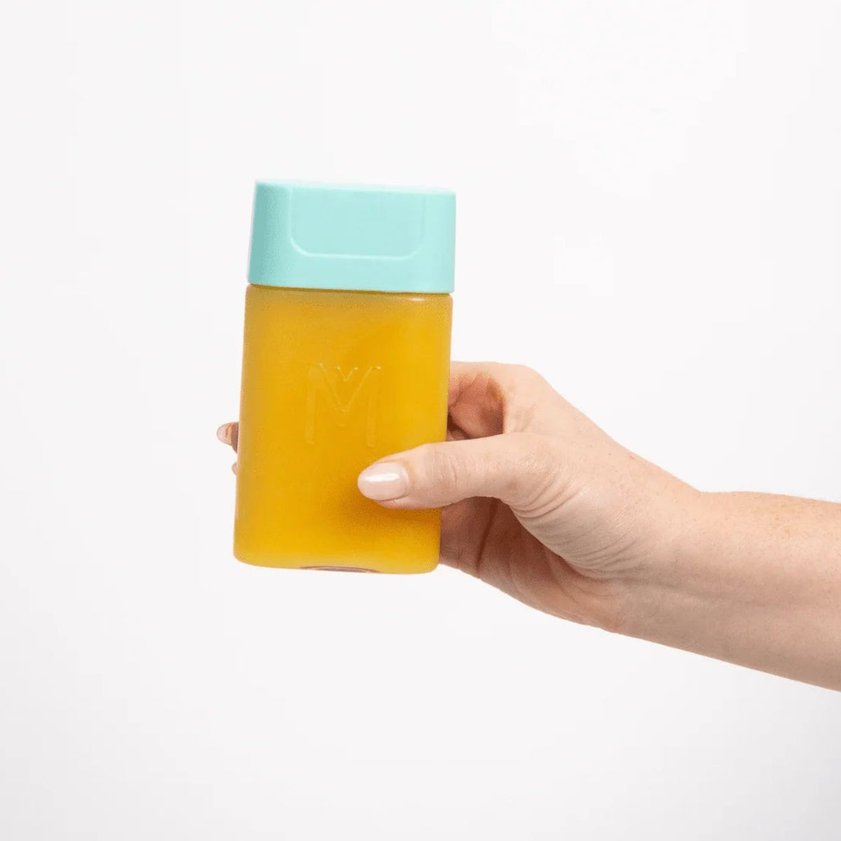 A hand holding a translucent yellow rectangular container with a light blue cap against a plain white background.