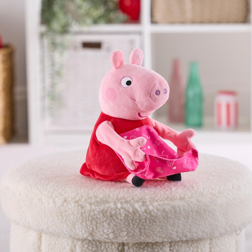 A Peppa Pig plush toy wearing a red dress and pink patterned skirt, sitting on a round white textured ottoman in a softly blurred indoor room setting.
