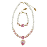 A matching pearl jewelry set featuring a necklace and bracelet with gold-tone hardware, pink faux pearls, a central pink gem, and a heart-shaped pendant with a cartoon character on a light gray background.