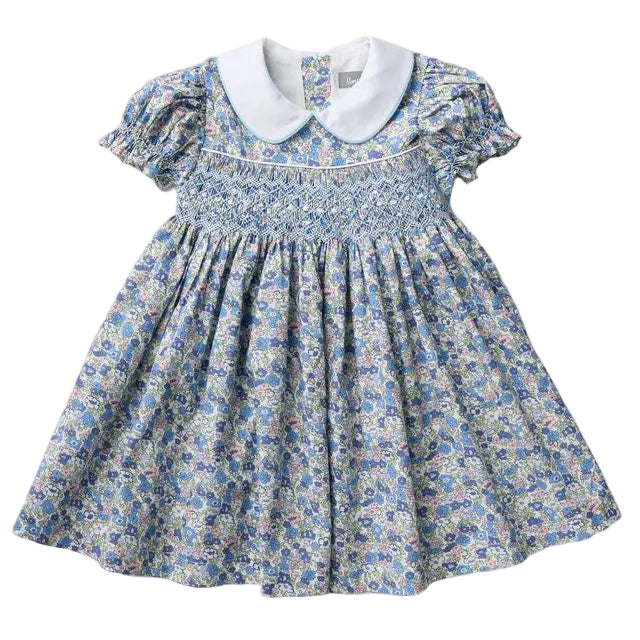 A toddler girl's smocked dress featuring a blue and white floral print, a white Peter Pan collar, and ruffled short sleeves, laid flat against a light gray background.