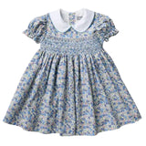 A toddler girl's smocked dress featuring a blue and white floral print, a white Peter Pan collar, and ruffled short sleeves, laid flat against a light gray background.