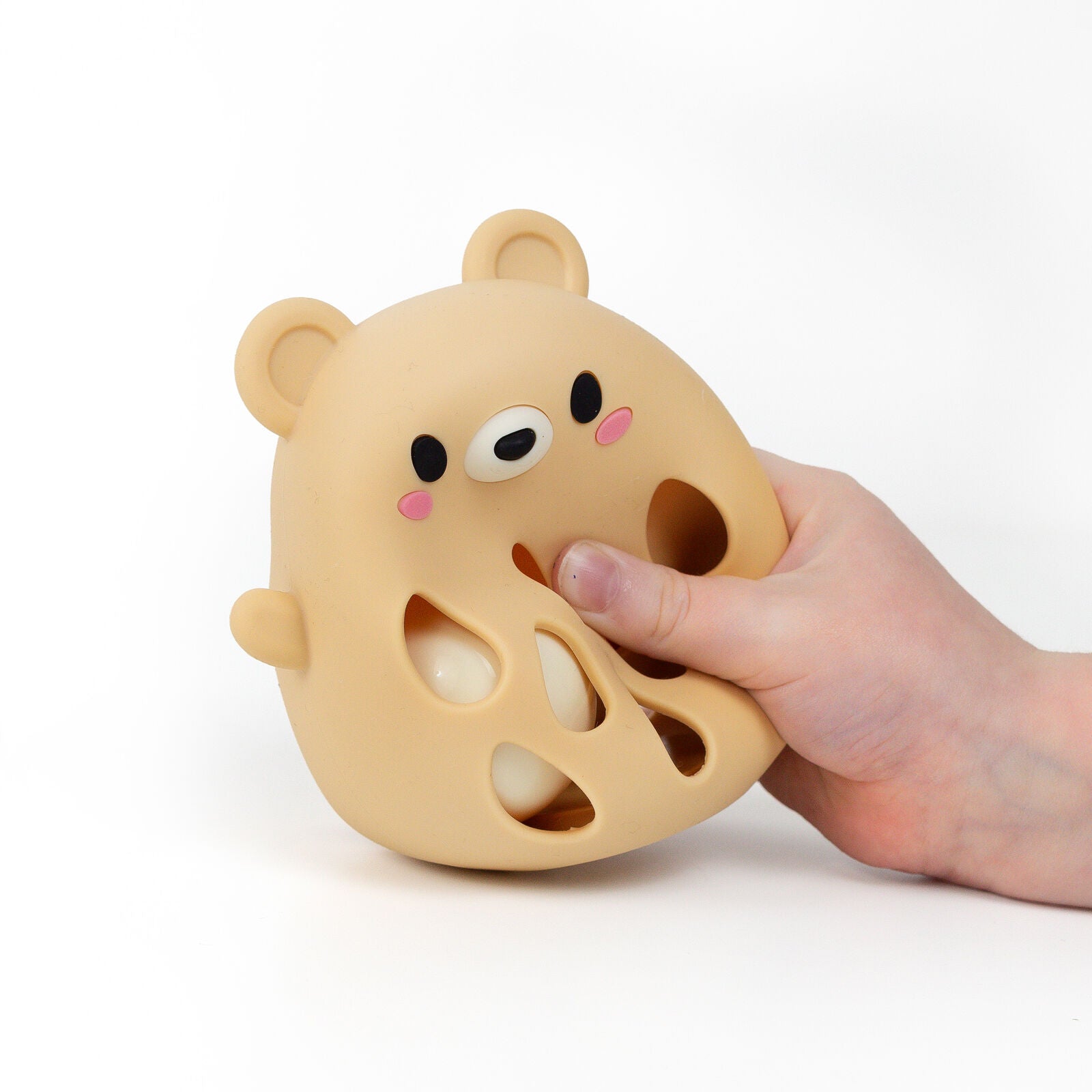 A cute bear-shaped silicone teething toy or bath mat in a warm beige/tan color, featuring a smiling face with black eyes, a white snout, pink cheeks, and cutout details on the body, shown on a plain white background.