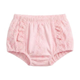A pair of light pink toddler bloomers with a textured, embroidered fabric and ruffle details on the sides, shown against a plain light gray background.