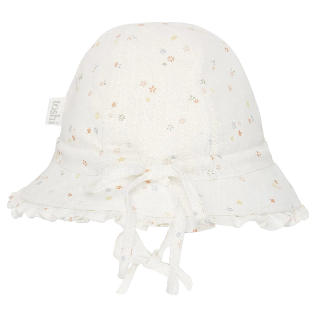 An off-white cotton bell baby bucket hat with a delicate multicolor floral print, featuring a ruffled brim, tie details, and a small side tag that reads 'baba+bi'.