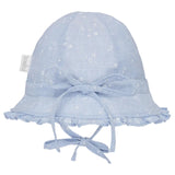 A light blue fabric baby sun hat with a white floral pattern, featuring a wide brim with ruffled trim, a matching bow on the front, and chin ties. A small fabric tag on the side reads 'loohi'.