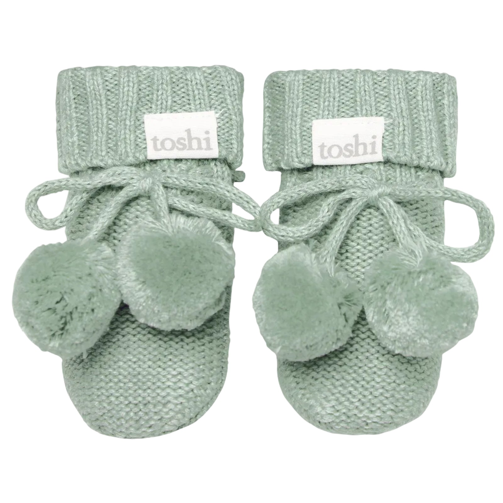Pair of green baby booties with pom-poms on a white background, featuring the brand 'toshi'.