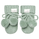 Pair of green baby booties with pom-poms on a white background, featuring the brand 'toshi'.