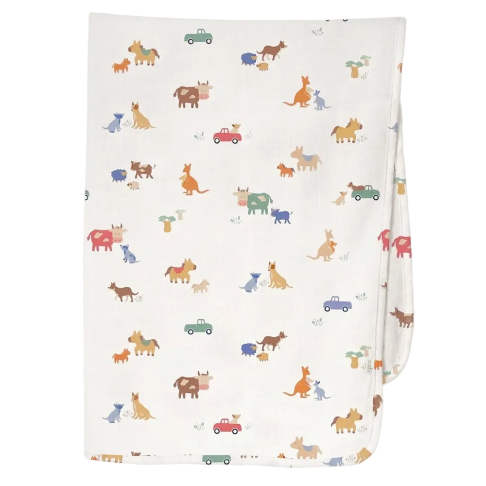 A folded white muslin blanket featuring a colorful cartoon animal print of dogs, cats, kangaroos, and small cars, shown against a light gray background.