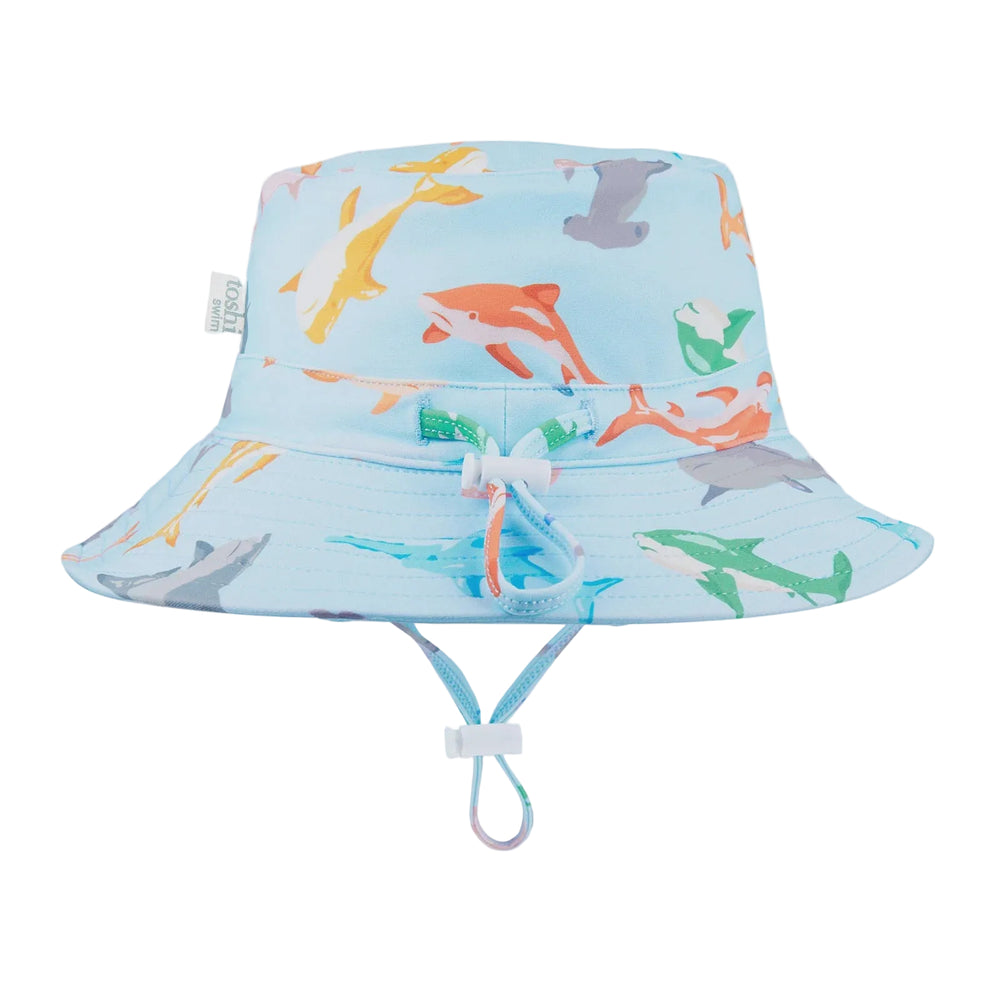 A blue and white baby sunhat with a shark pattern, featuring a head tie and chin strap for adjustable fitting, labeled with 'UPF50+' for sun safety.