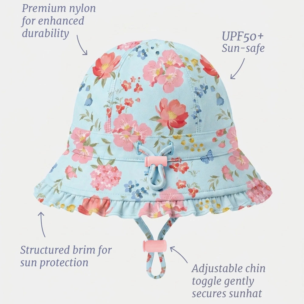A light blue floral bucket swim sun hat with pink, red, and yellow flowers, shown with text callouts highlighting its features: premium nylon durability, UPF50+ sun safety, structured brim, and adjustable chin toggle.