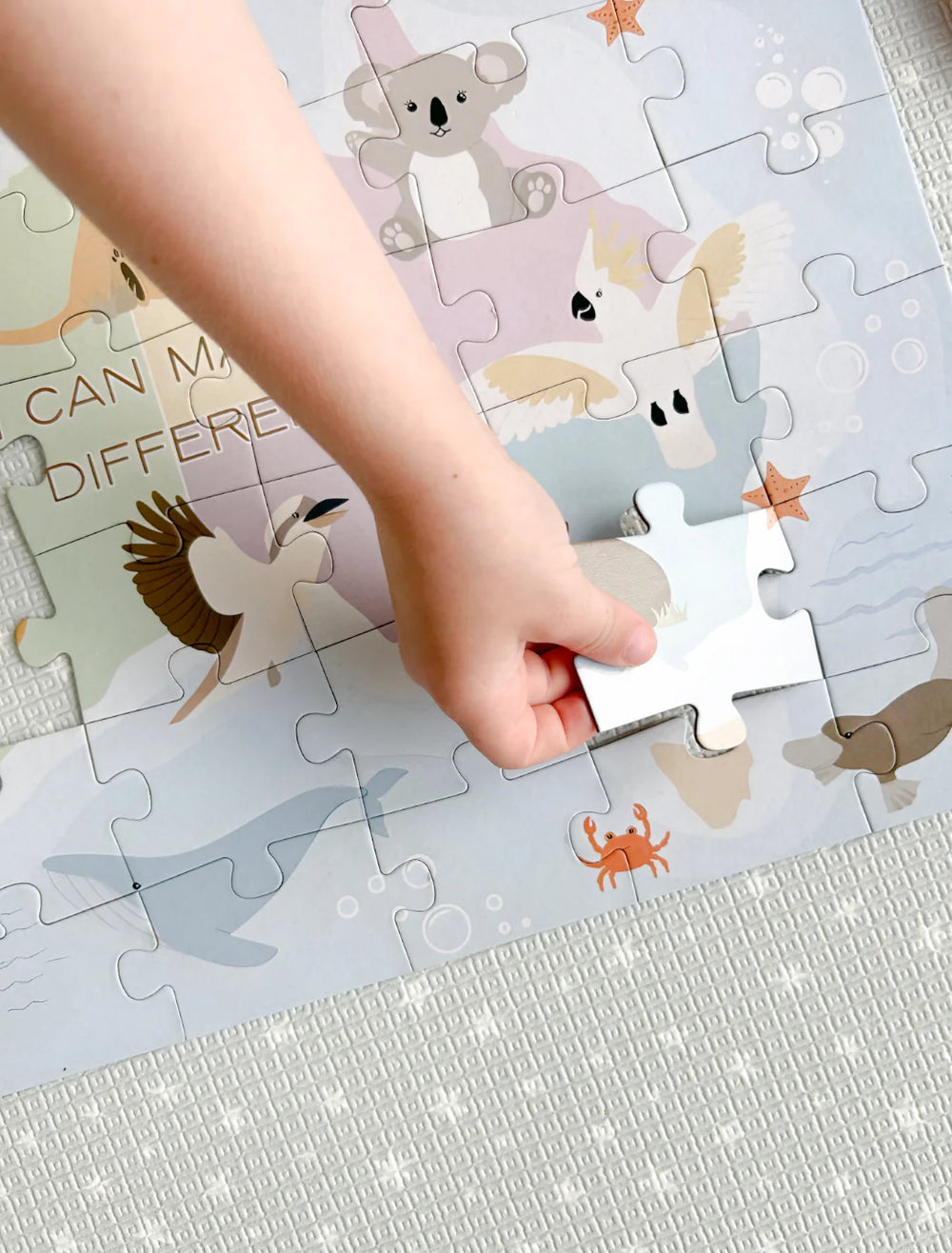 Child's hand placing a puzzle piece on an animal-themed puzzle.