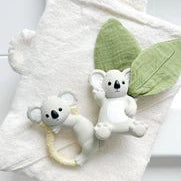 Two small Koala toys on a white towel with green fabric leaves attached to one koala
